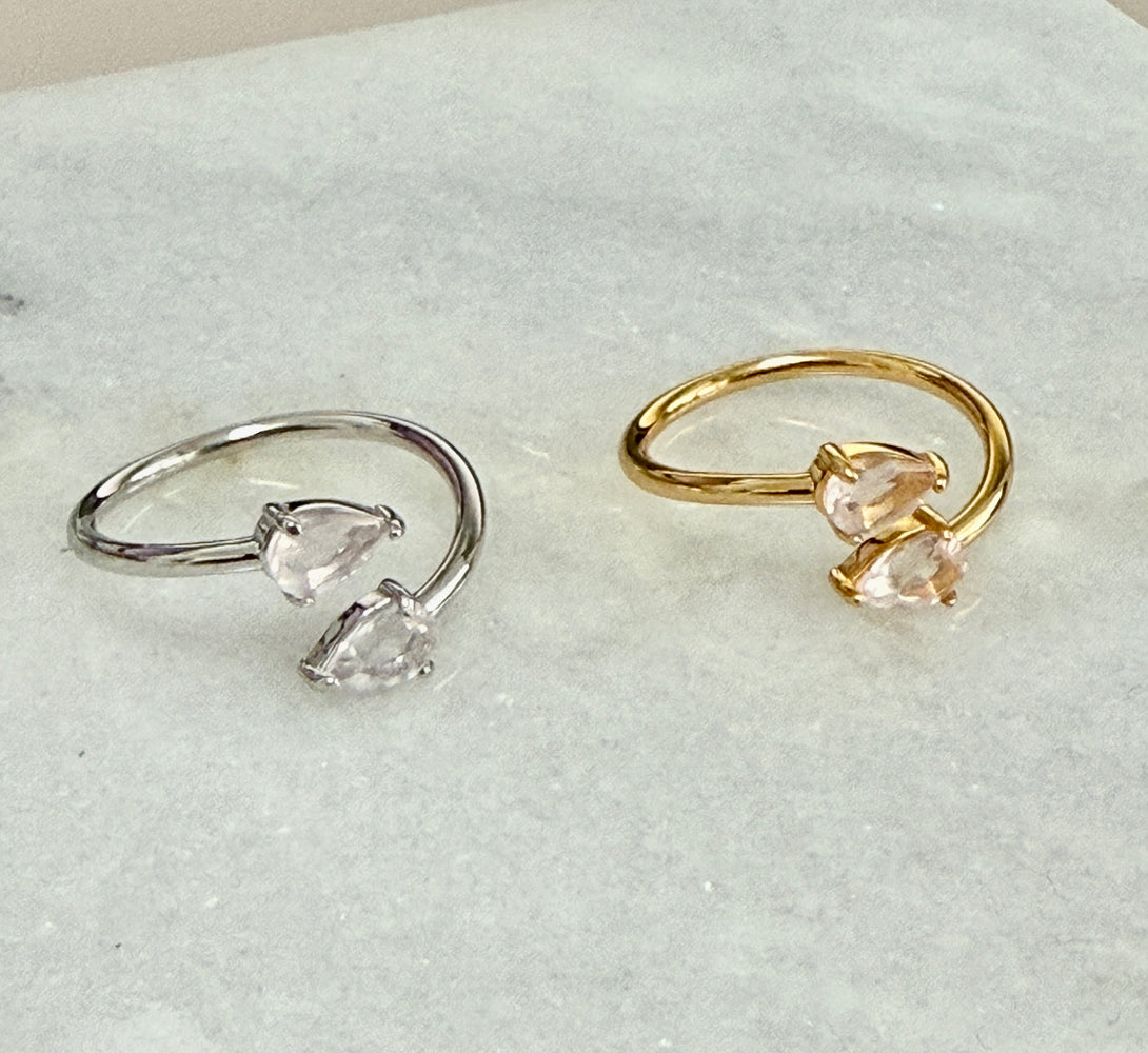 Two rings featuring rose quartz gemstone, one 18k gold and one sterling silver on a marble background
