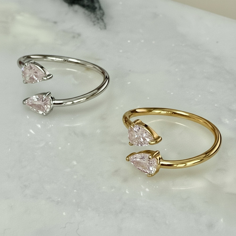 Two open gold and silver rings with teardrop-shaped gemstones on a marble surface.