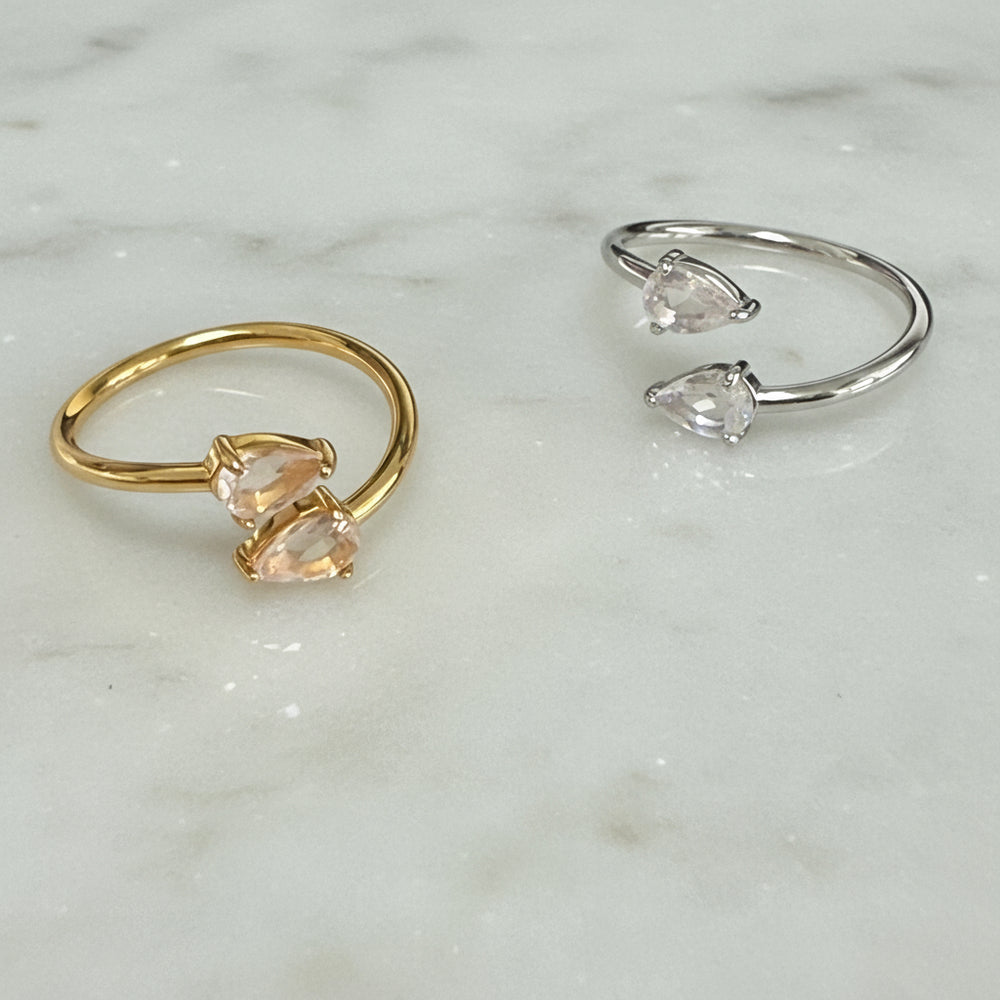 Two rings, one gold and one silver, with teardrop-shaped gemstones on a light gray background.