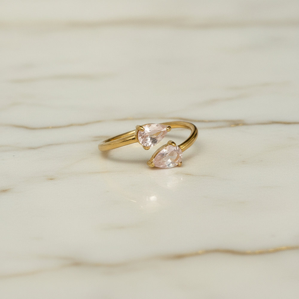 Gold ring with two pink gemstones on a white marble background