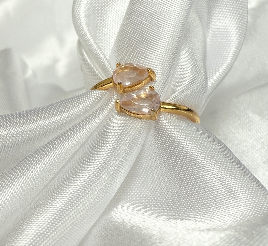 Gold ring with two pink quartz gemstones on a white satin background