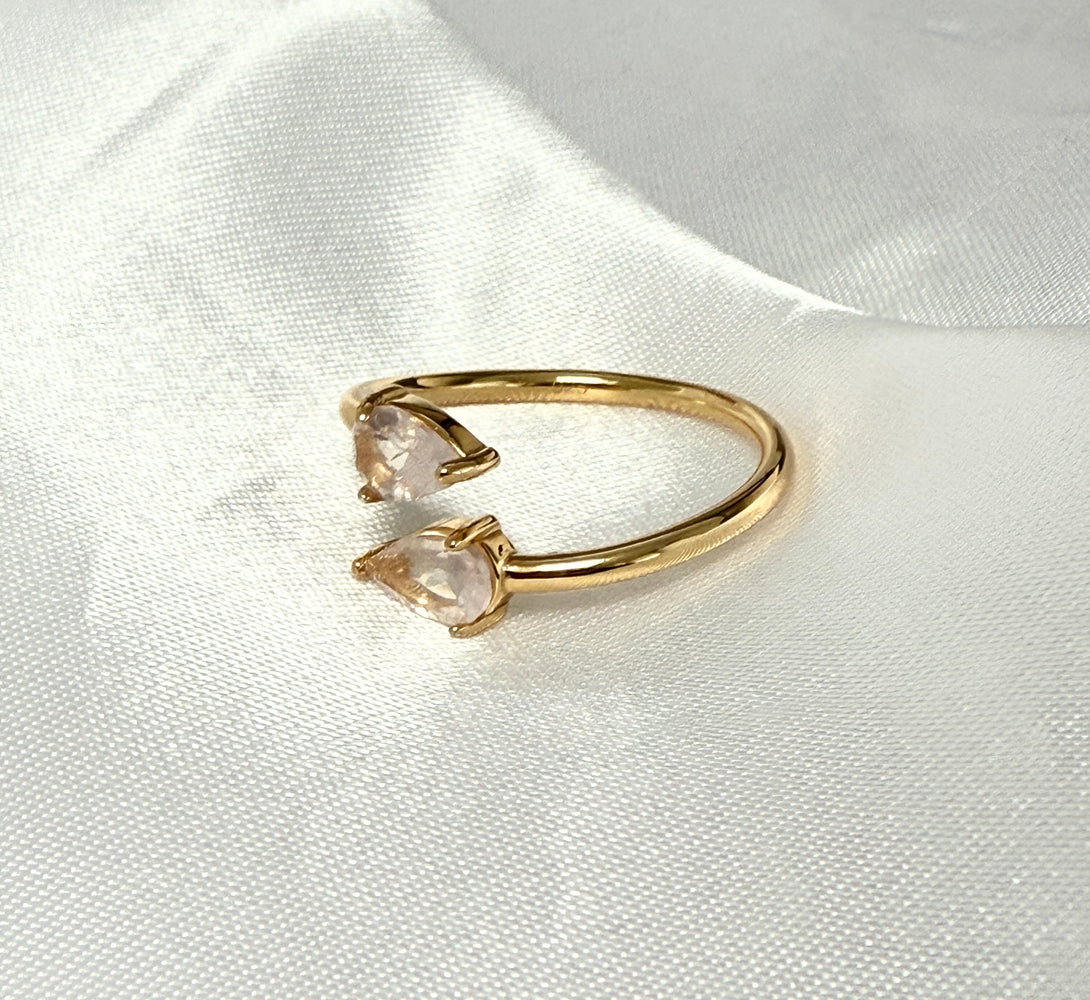 Gold ring with two teardrop-shaped gemstones on a white satin background
