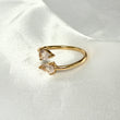Gold ring with two teardrop-shaped gemstones on a white satin background