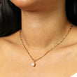 Gold chain necklace with a pearl pendant on a person's neck with crystal detail